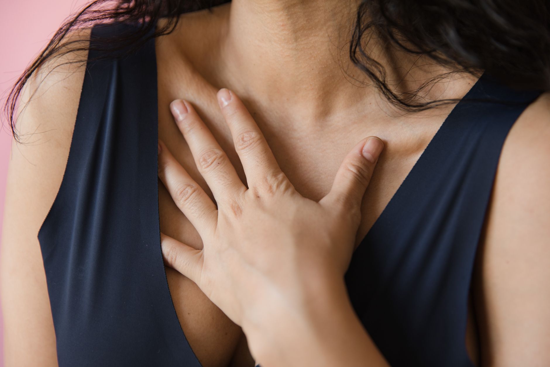 Intimate close-up of a woman in a sleeveless blue top with a hand on her chest, conveying emotion.