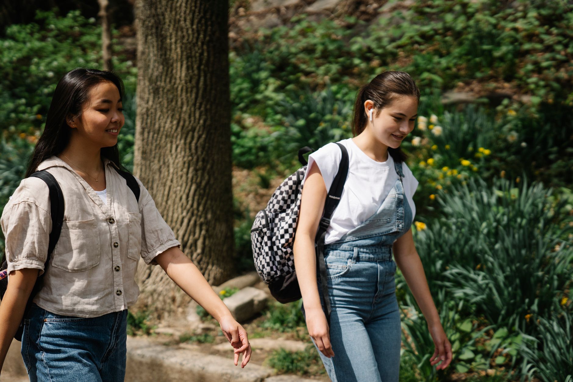 Two teenage girls walking outdoors with backpacks, enjoying a sunny day after school.