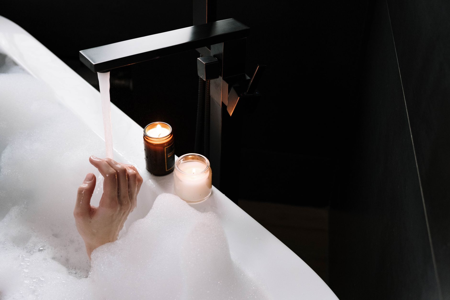 A comforting bubble bath scene with lighted candles, showcasing a hand and running water for a tranquil atmosphere.