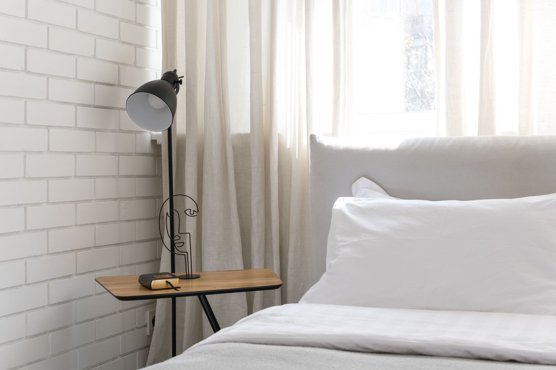 Inviting minimalist bedroom interior with a cozy atmosphere, featuring a soft bed and elegant side lamp.