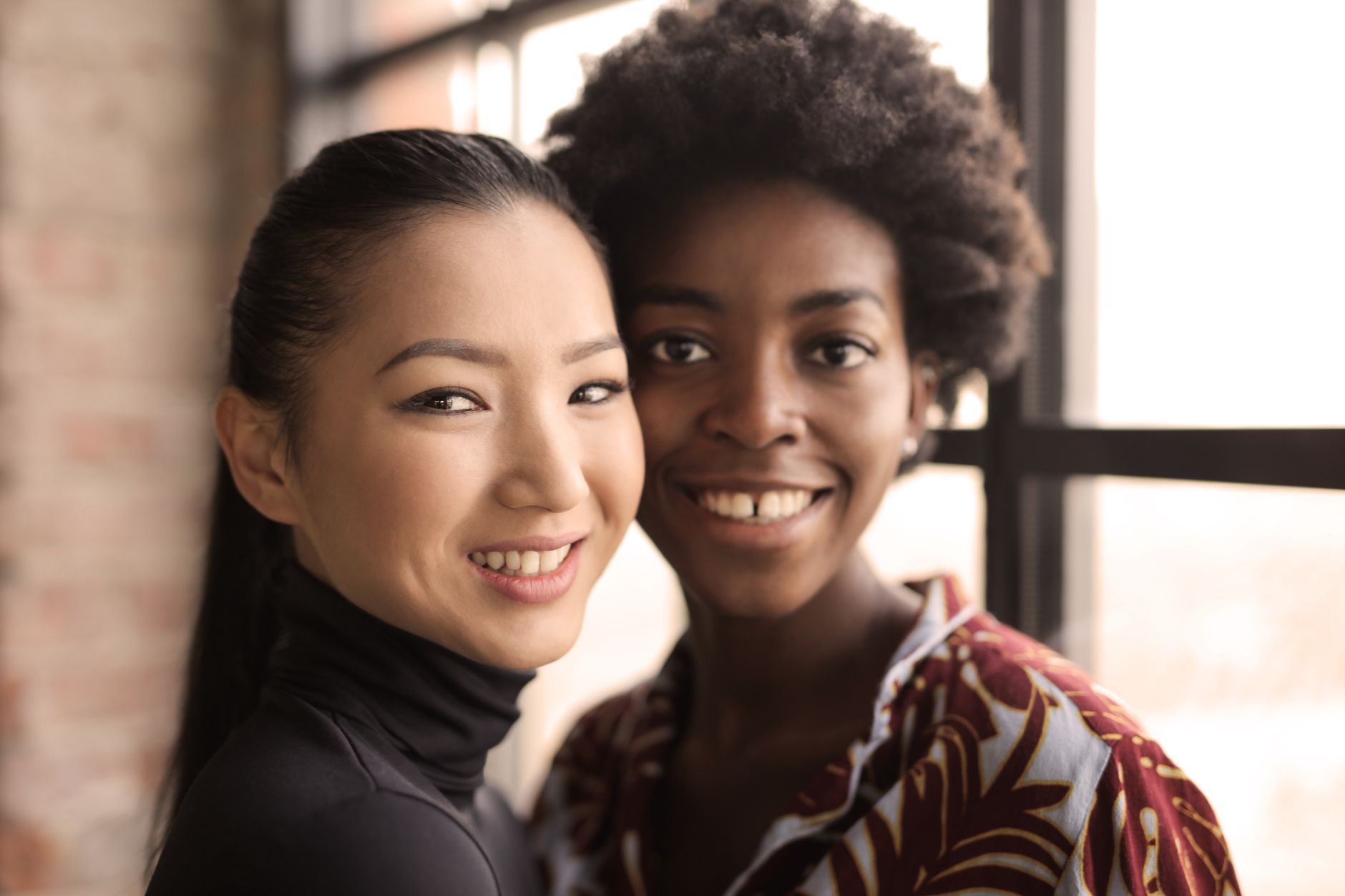Close-up of two diverse women smiling together indoors, exuding happiness.
