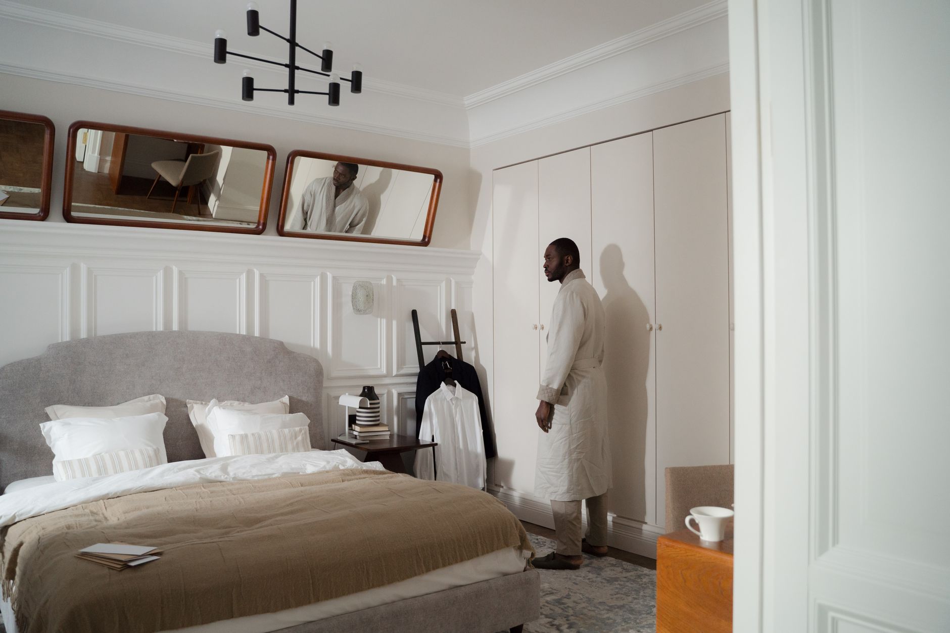 A man in a bathrobe stands in a modern, stylish bedroom with neutral tones.