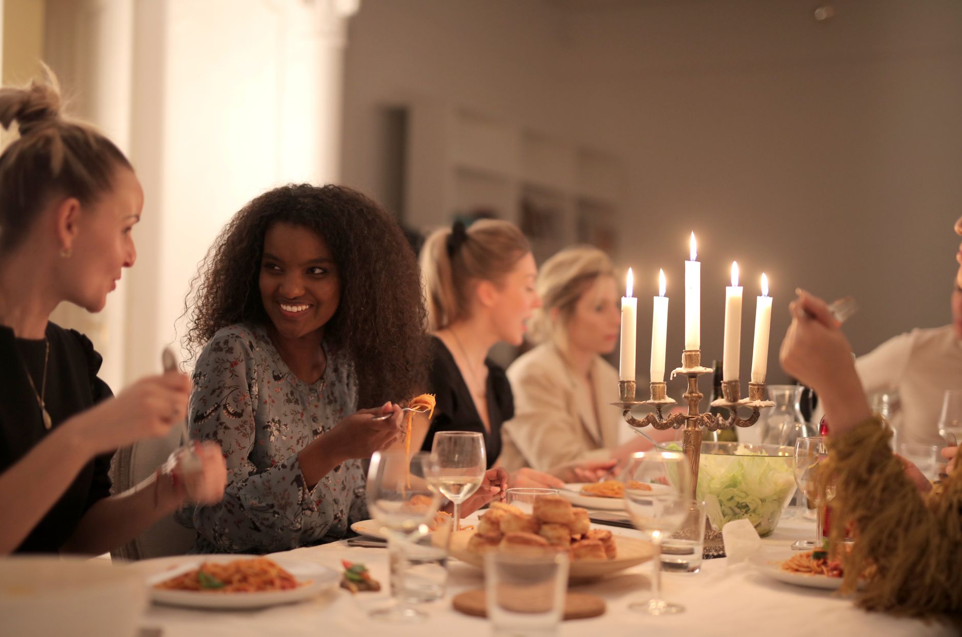 A group of diverse friends enjoying a candlelit dinner, sharing laughter and wine, indoors.
