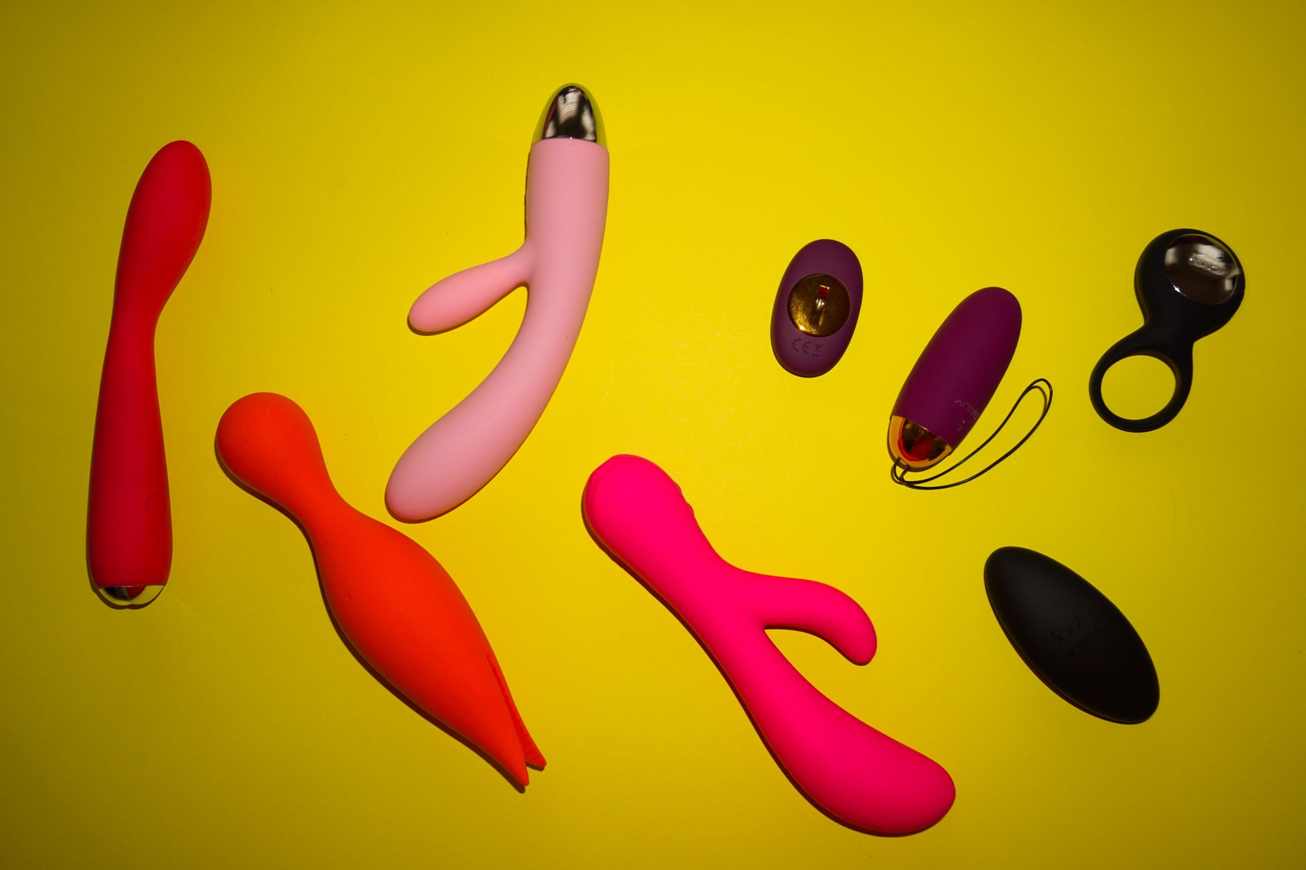 Vibrant photo of various sex toys arranged on a bright yellow surface, showcasing diversity and design.