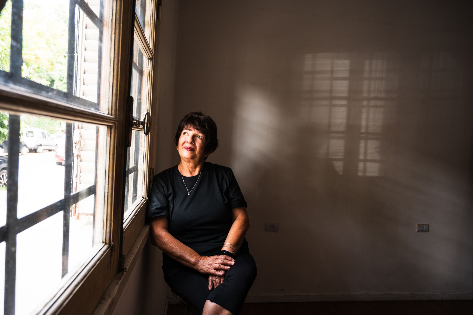 A thoughtful senior woman sitting by a window in a softly lit room, lost in contemplation.