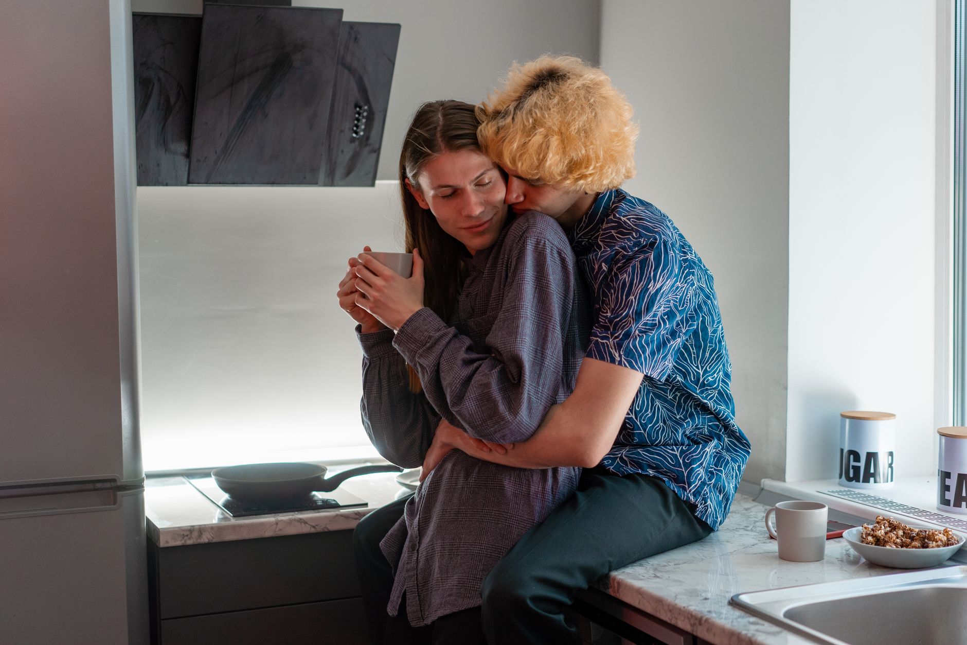 An affectionate couple enjoys a tender moment in a modern kitchen setting.