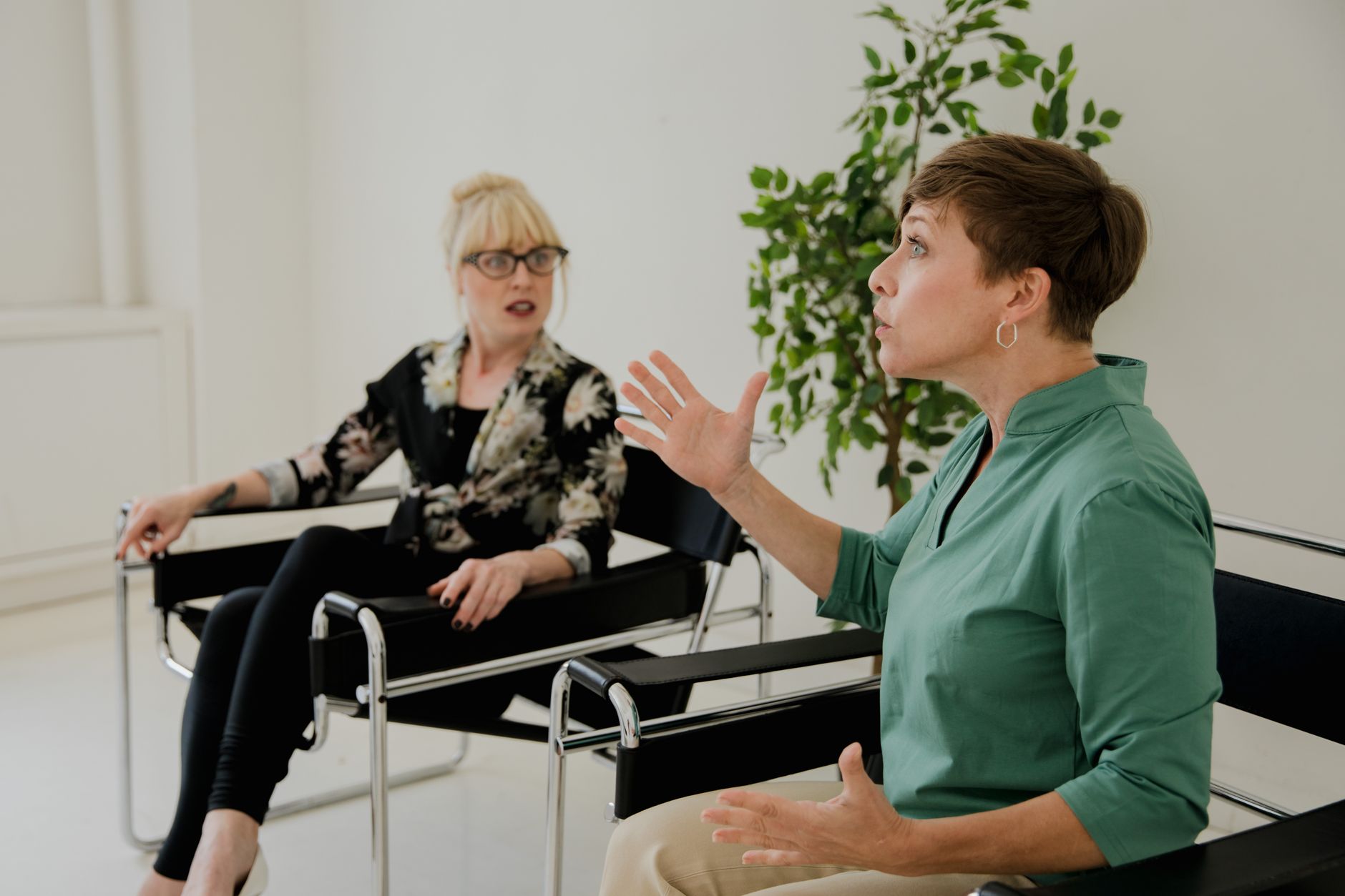 Two women engaged in a serious discussion in a modern office setting, highlighting communication and mental health.