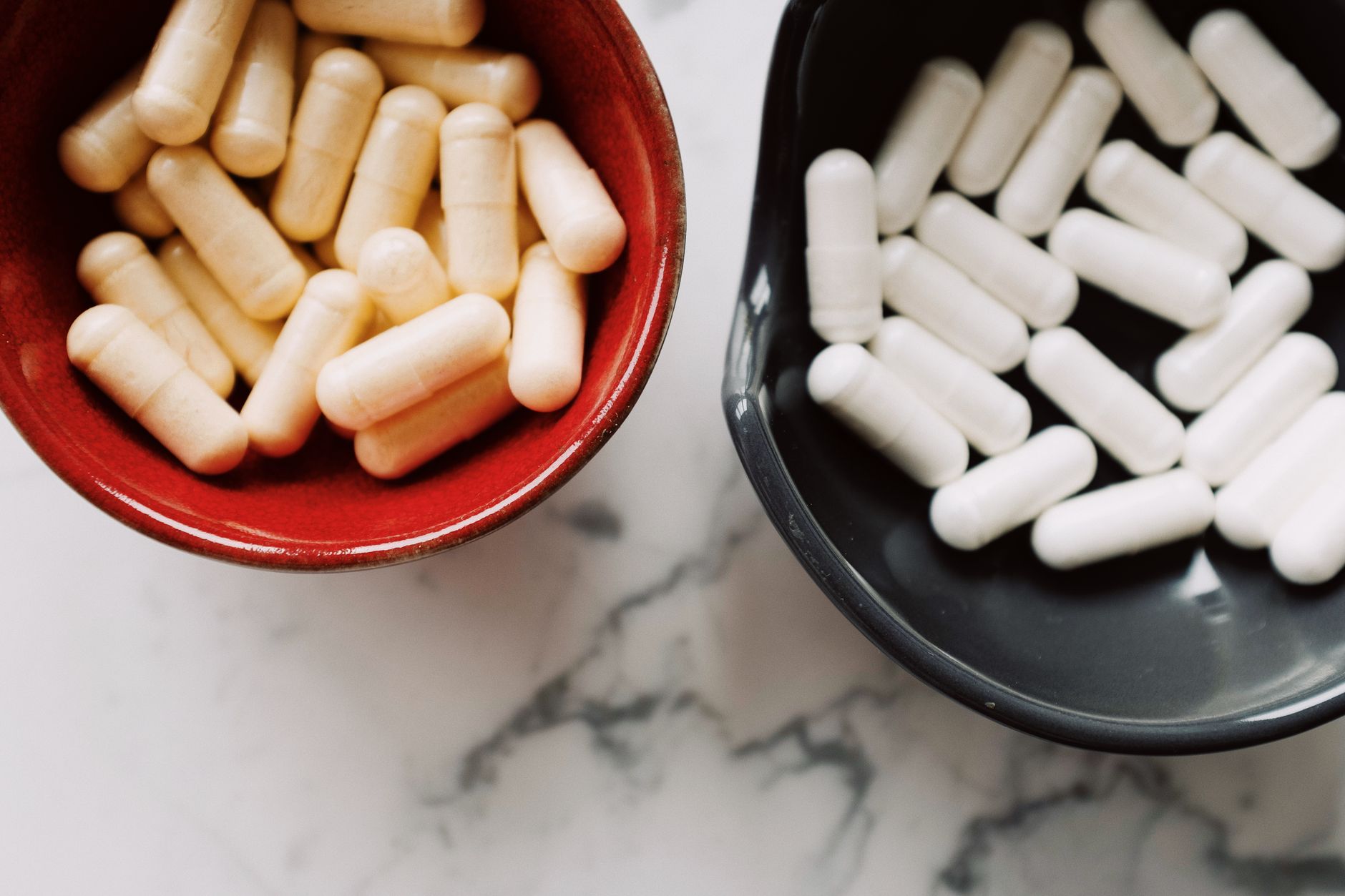 Two bowls with capsules on a marble surface, representing healthcare or medicine concepts.