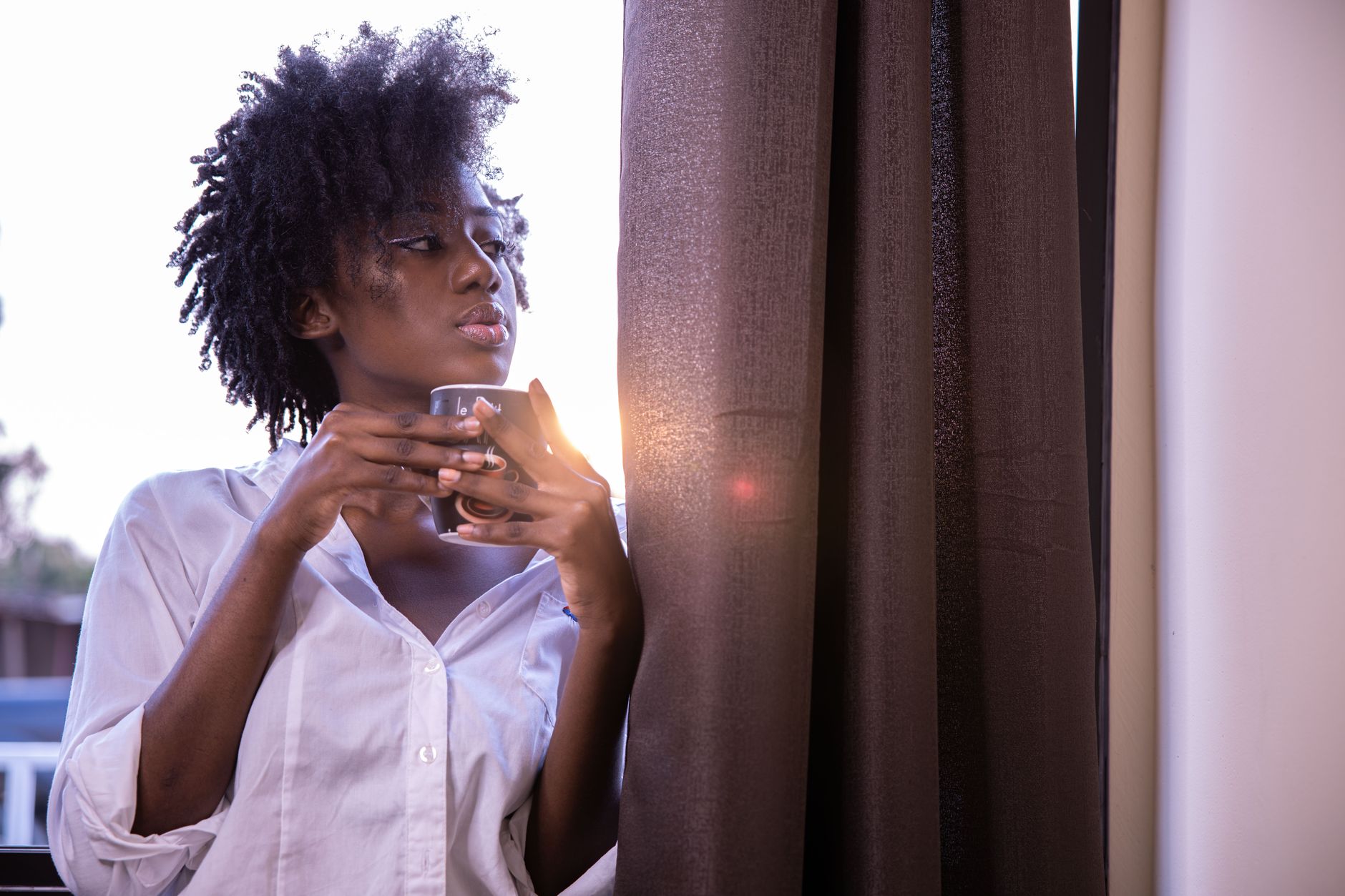 A woman enjoys a peaceful moment by the window with a hot coffee cup.