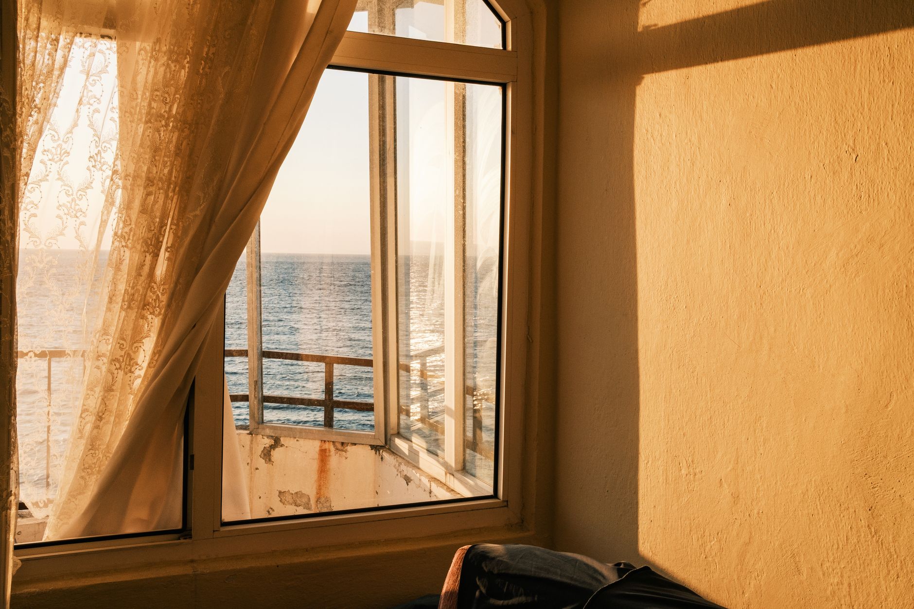 Sunlight streaming through a lace curtain reveals a tranquil ocean view, reflecting warmth and calm.