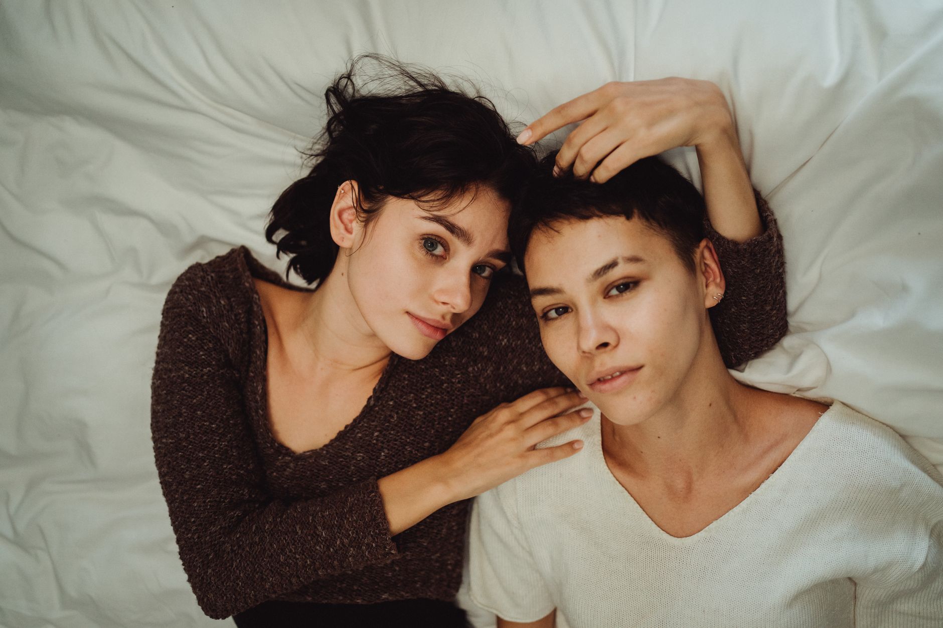 A tender moment between two women lying together on a bed, showcasing intimacy and connection.