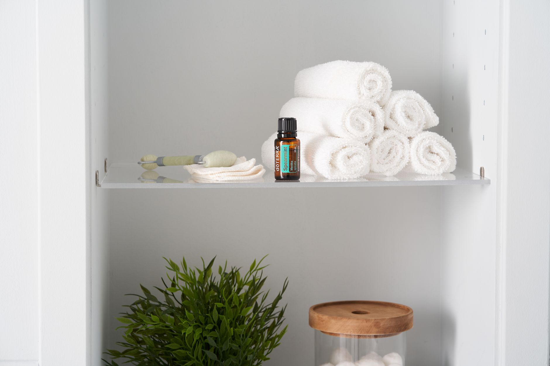 Neatly folded towels with essential oil and jade roller on a shelf for a relaxing spa ambiance.